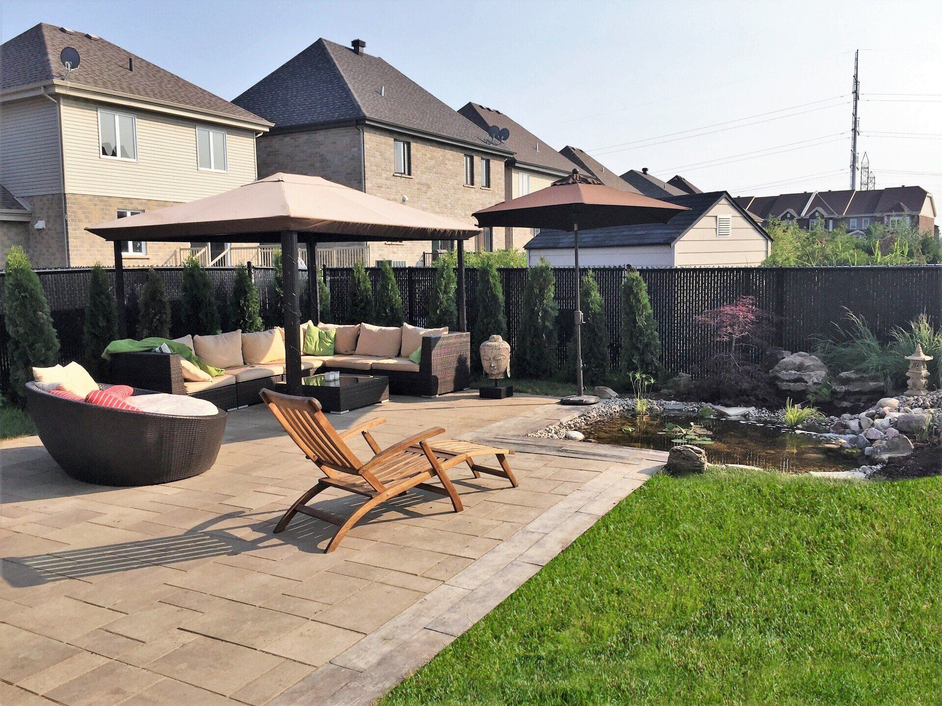 Terrasse avec chaises longues, parasol et un petit bassin bordant une pelouse verdoyante dans une cour arrière de banlieue