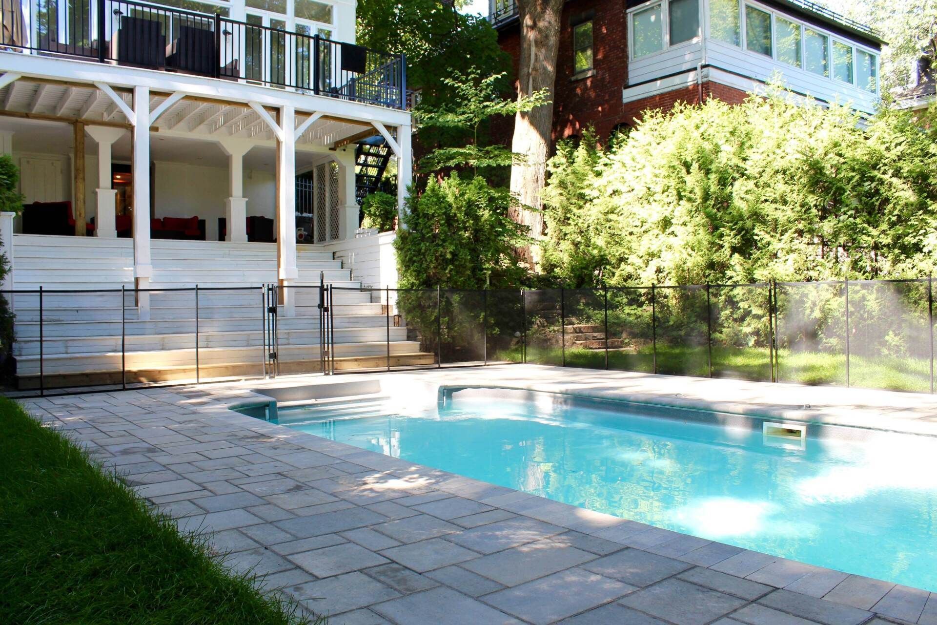 Piscine dans le jardin d'une maison blanche avec véranda ombragée et terrasse en pierre