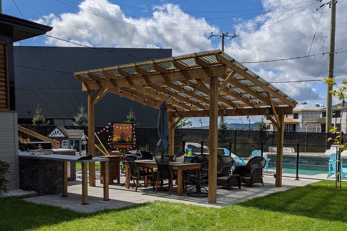Terrasse arrière avec pergola en bois, sièges extérieurs, barbecue et piscine sous un ciel bleu