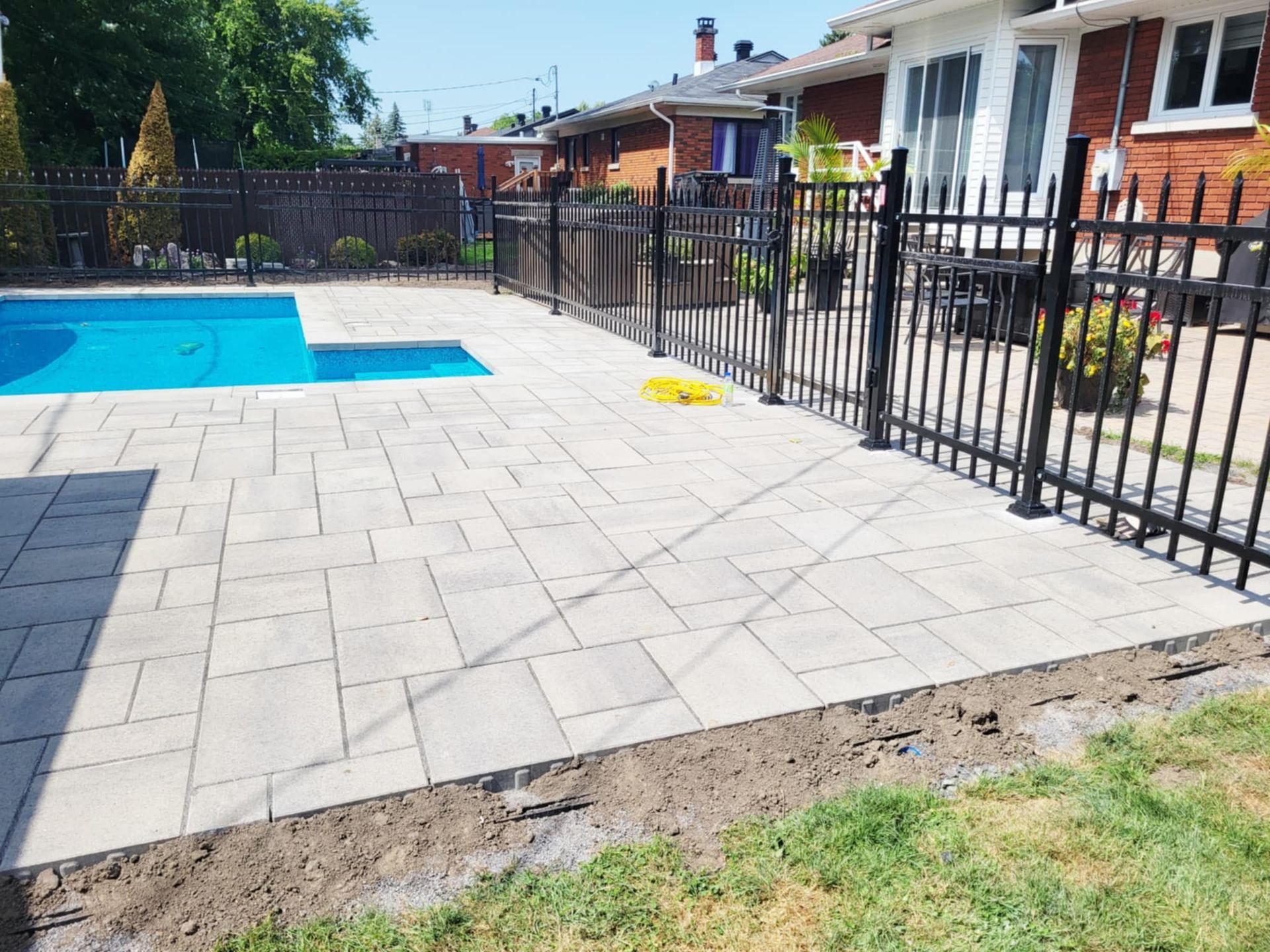 Terrasse arrière avec pavés gris, piscine bleue et clôture en métal noir à côté d'une maison