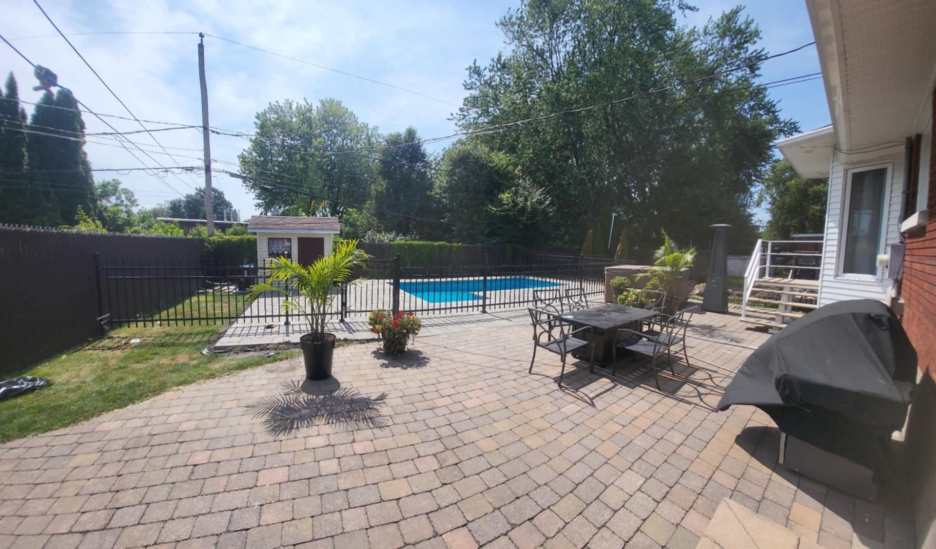 Terrasse arrière avec plantes en pot, barbecue, table et piscine par une journée ensoleillée