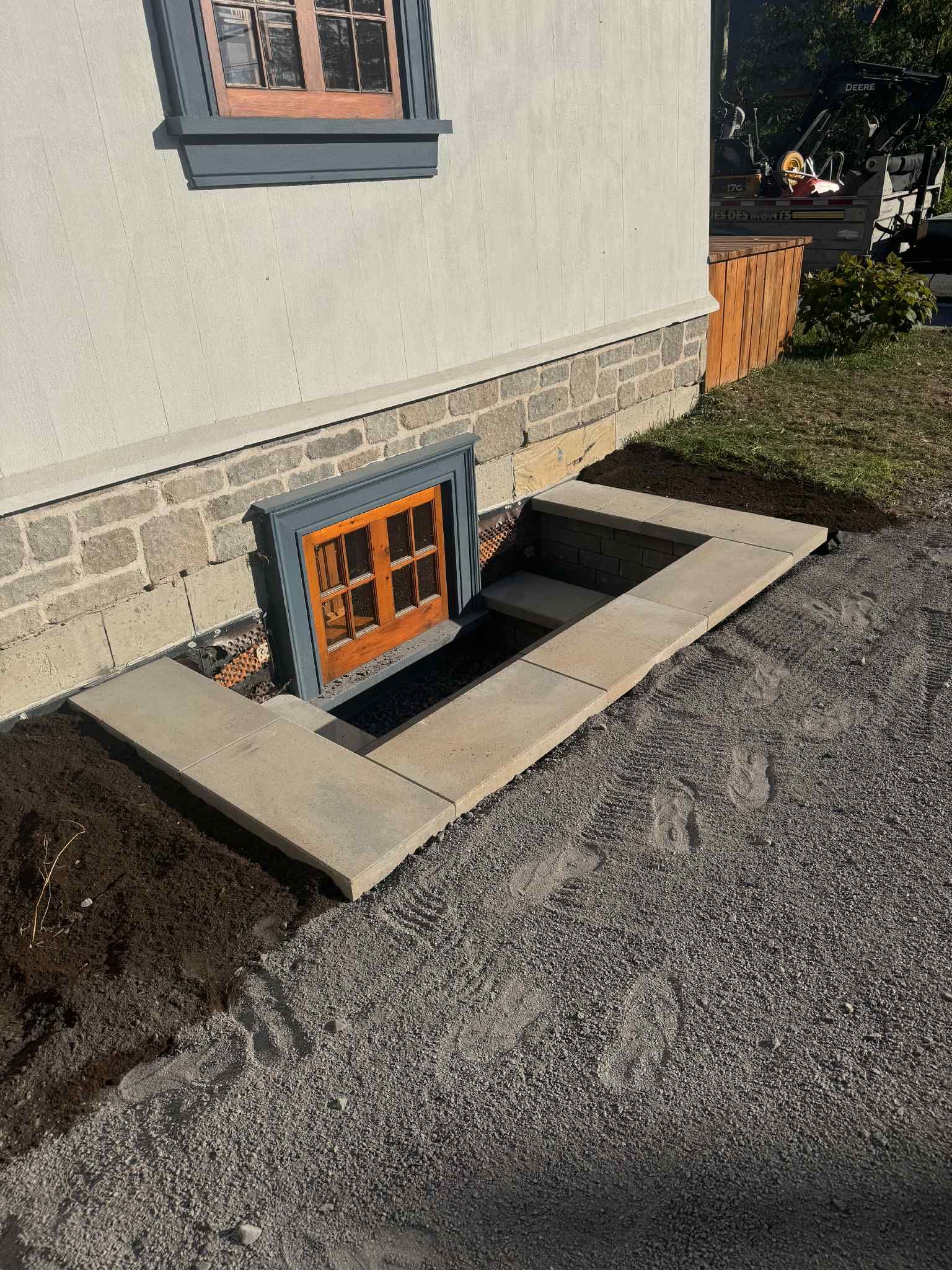 Puits de lumière en sous-sol avec marches en béton et petite fenêtre à cadre orange à côté d'une maison.