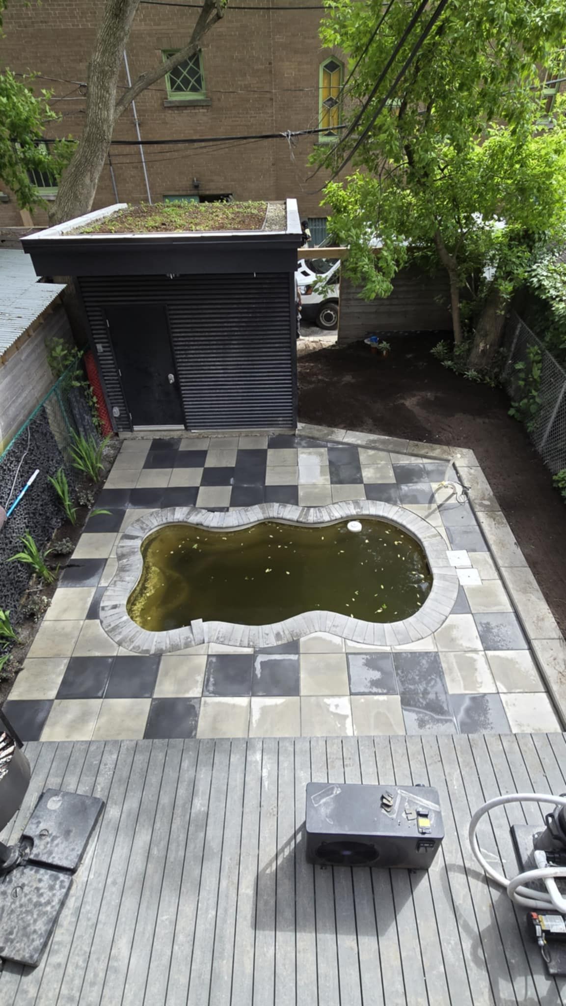 Petit patio avec un bassin, des dalles de pierre, de la verdure et un abri couvert à l'arrière.