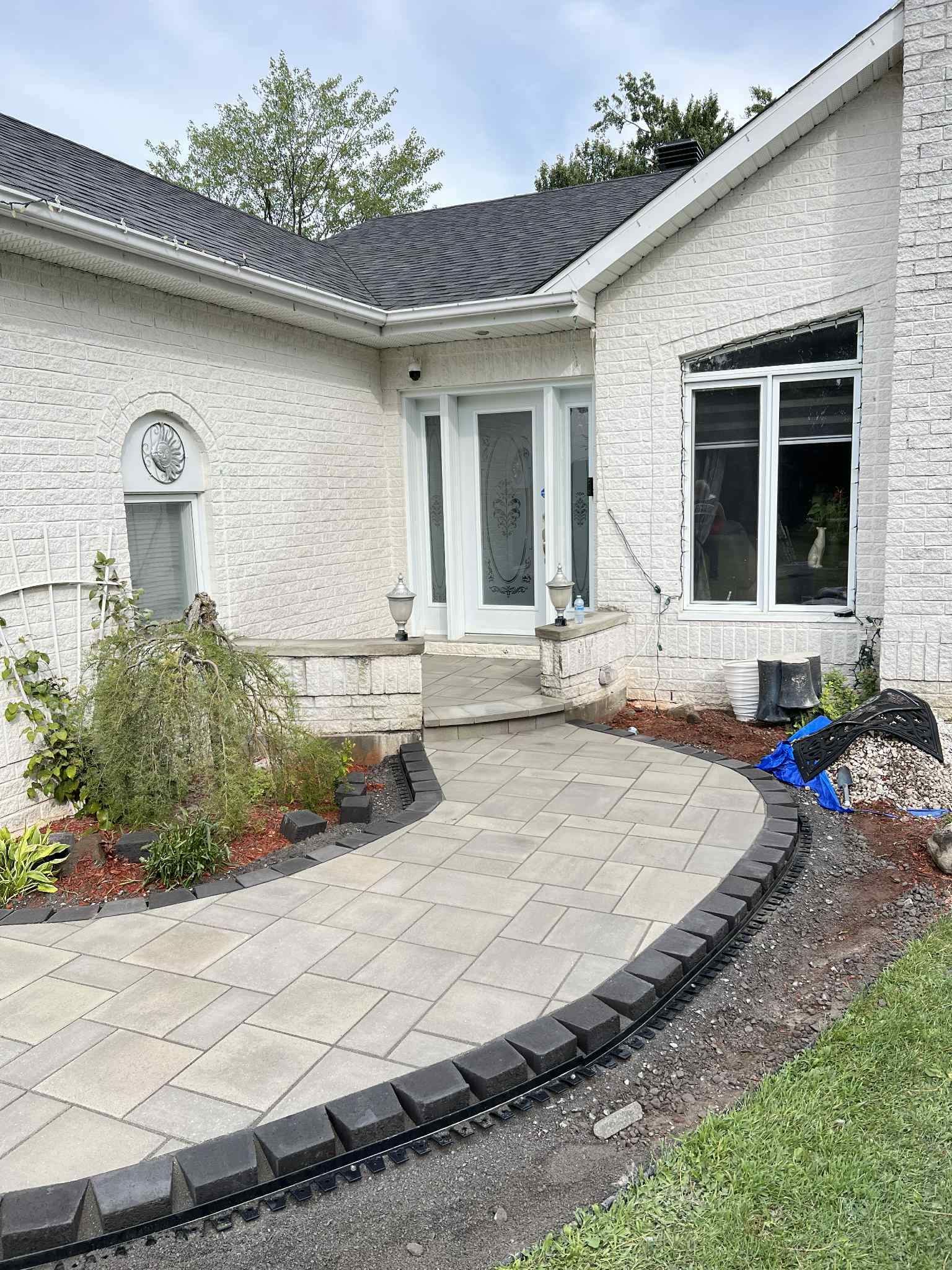 Entrée principale d'une maison en briques blanches avec allée en pierre incurvée et petit jardin paysager