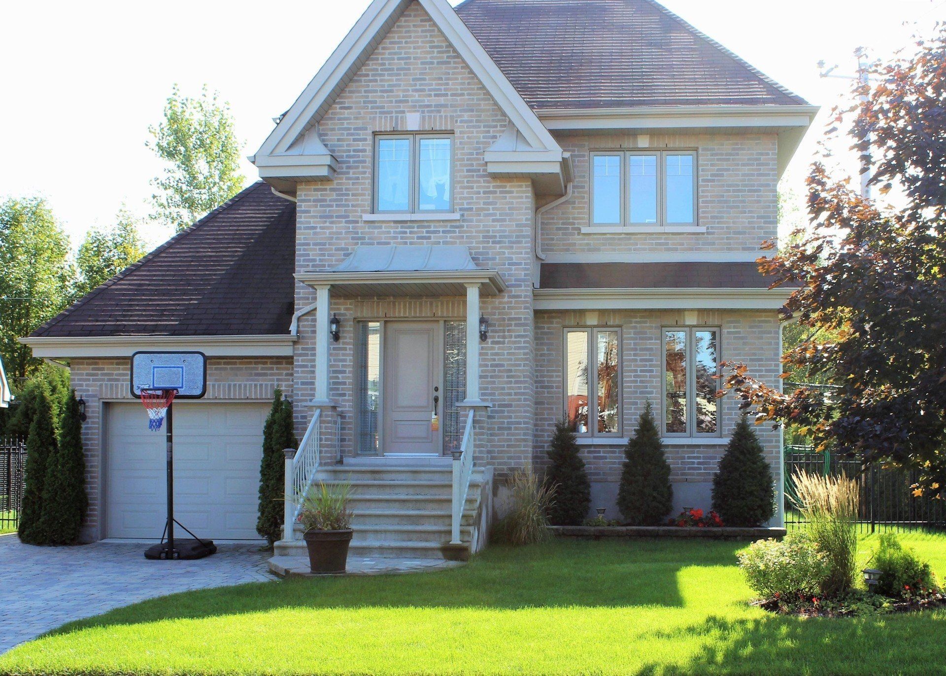 Maison de banlieue avec façade en pierre, perron, garage et panier de basket dans l'allée.
