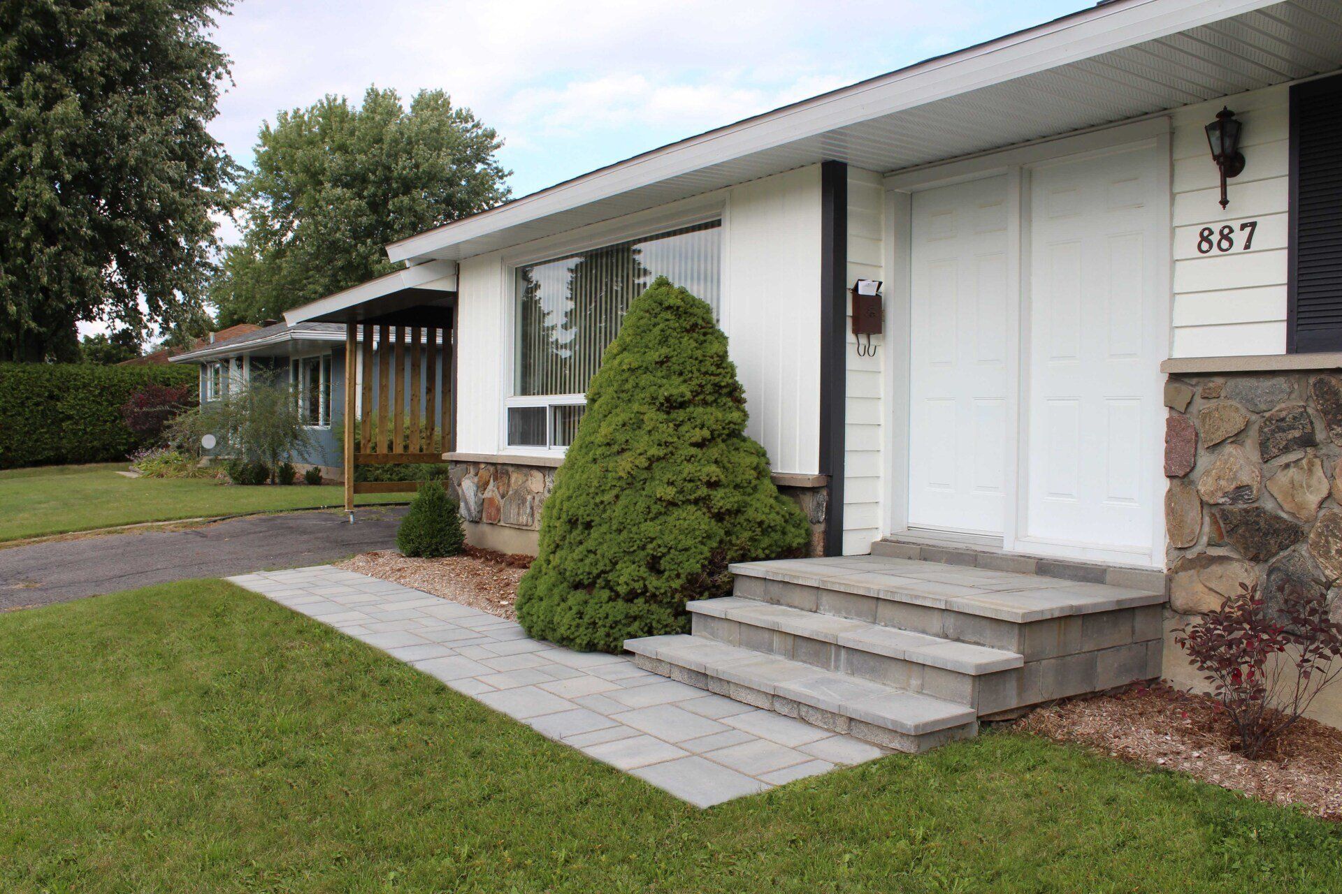 Suburban house entrance with white doors, stone steps, and a green lawn