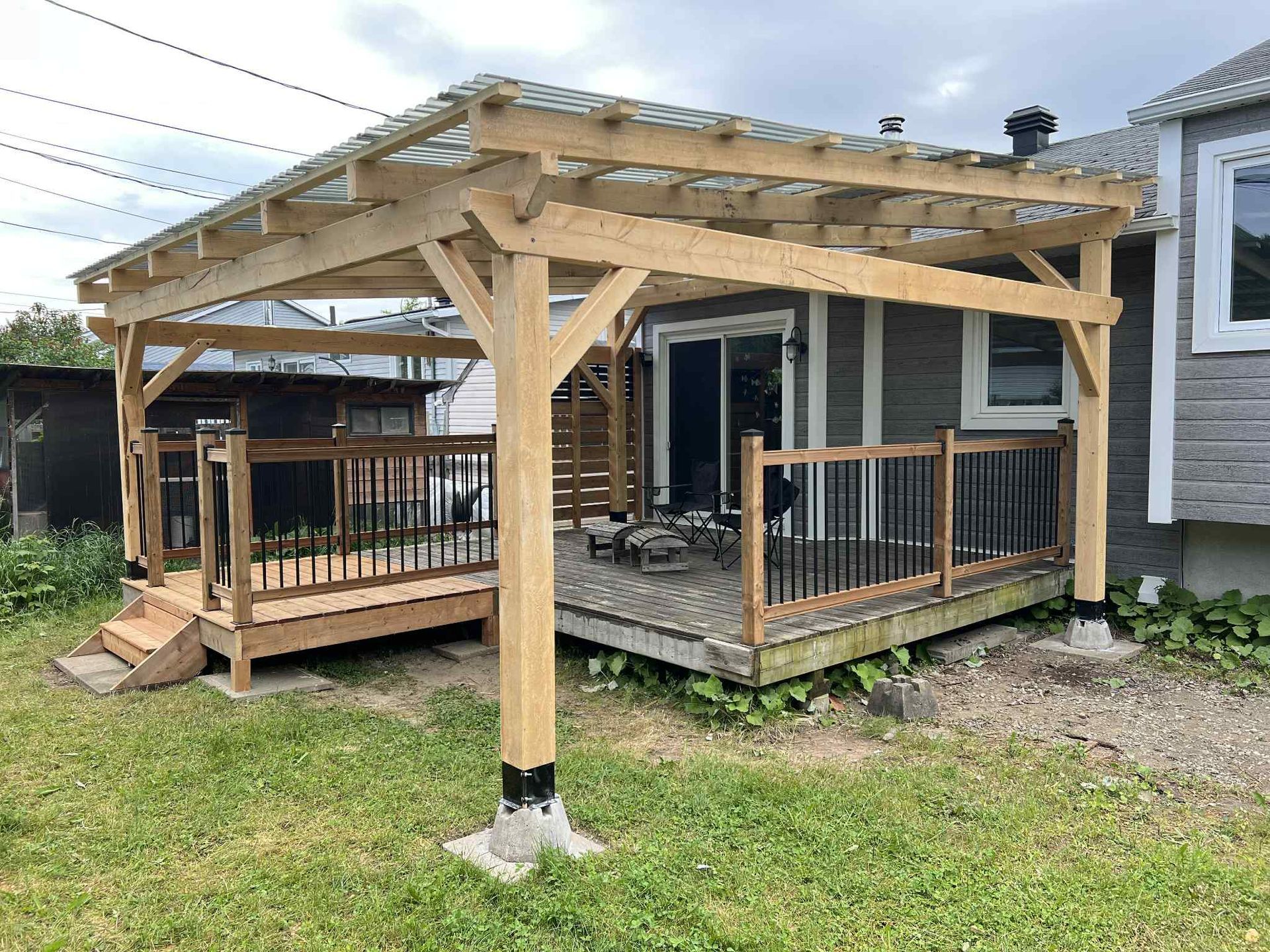 Terrasse en bois avec pergola et rambarde, attenante à une maison et donnant sur un jardin gazonné.