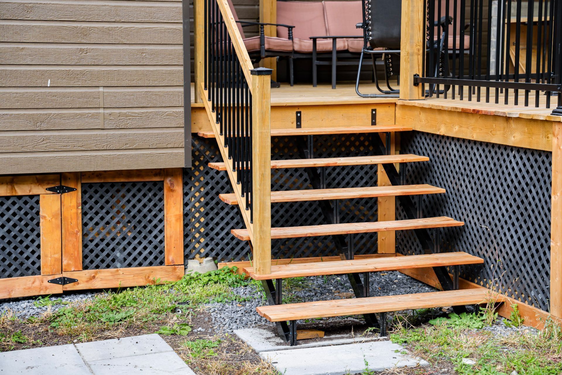 Des marches d'escalier en bois avec rambarde mènent à une terrasse attenante à une maison dotée d'une plinthe en treillis.