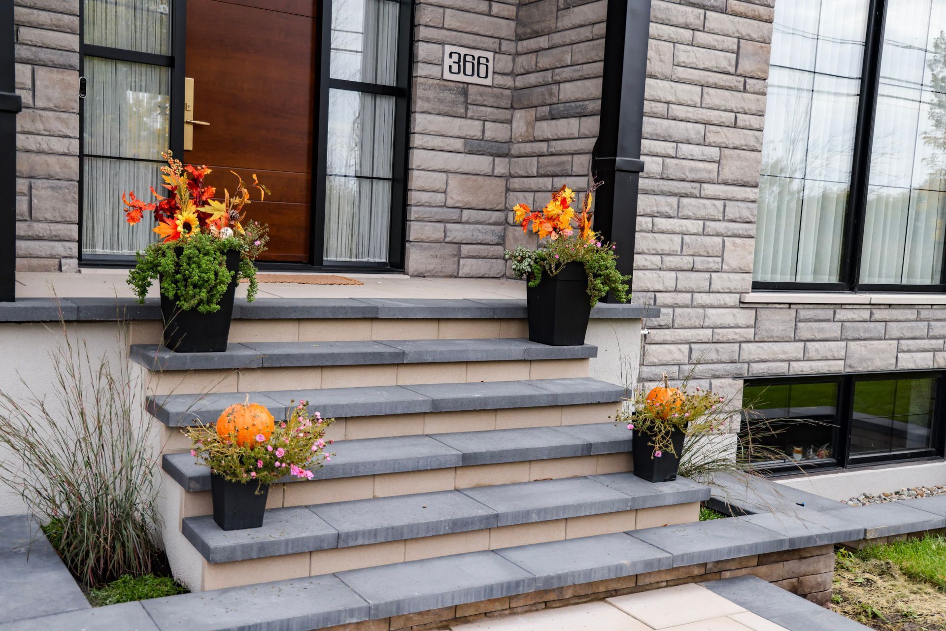 Les marches d'entrée en pierre de la maison sont ornées de jardinières noires à fleurs orange près de la porte.