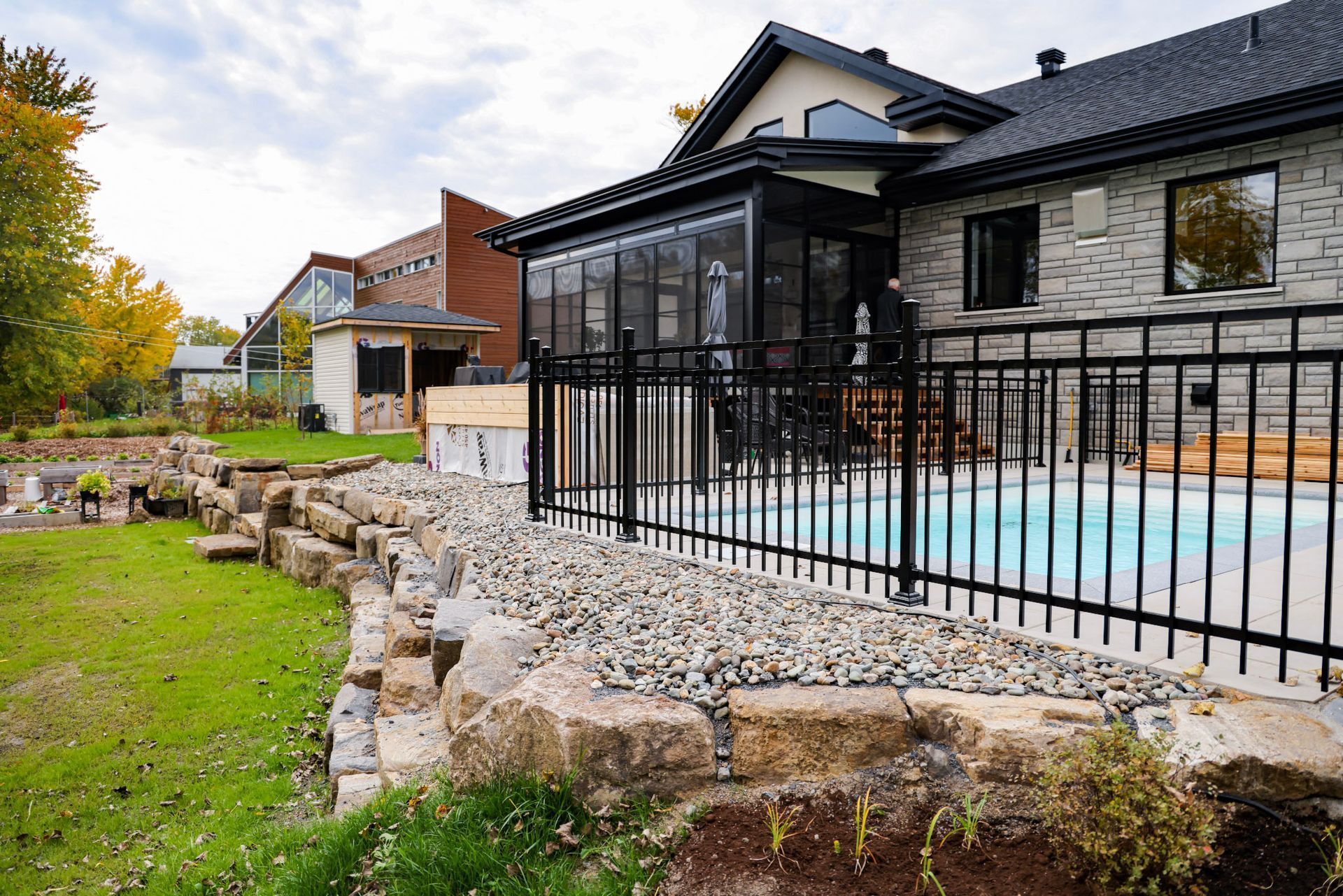 Maison en pierre avec une clôture noire à côté d'une piscine et d'un jardin paysager au crépuscule