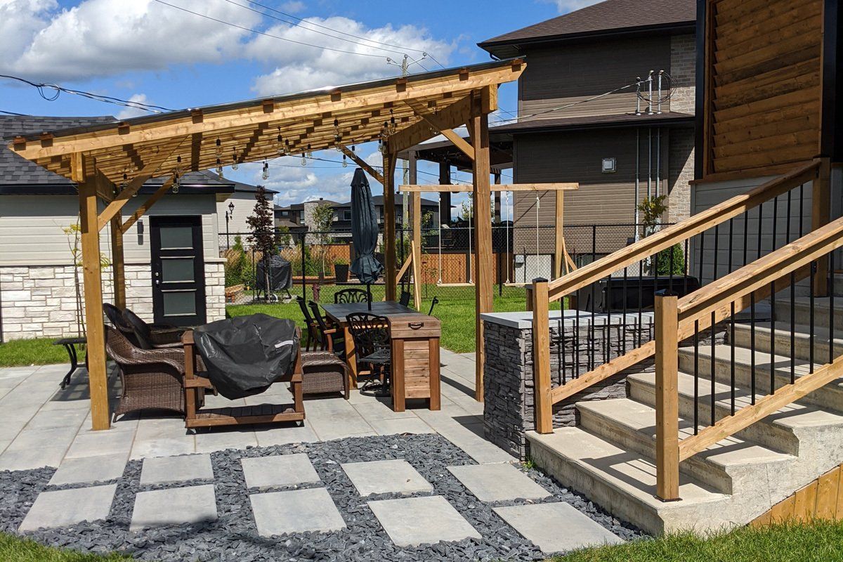 Terrasse arrière avec pergola, dalles de pierre et escalier à côté d'une maison sous un ciel bleu