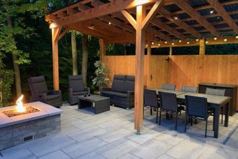 Terrasse couverte avec foyer, sièges en osier foncé et table à manger sur dalles de pierre au crépuscule
