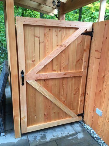 Portail de jardin en bois avec traverses diagonales et loquet noir, installé entre des panneaux de clôture sous un patio couvert.