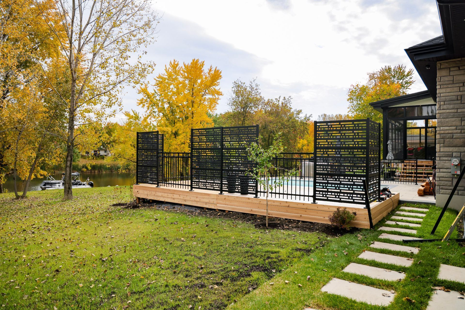 Terrasse arrière avec piscine, balustrade en métal noir et arbres aux couleurs d'automne à côté d'une maison moderne
