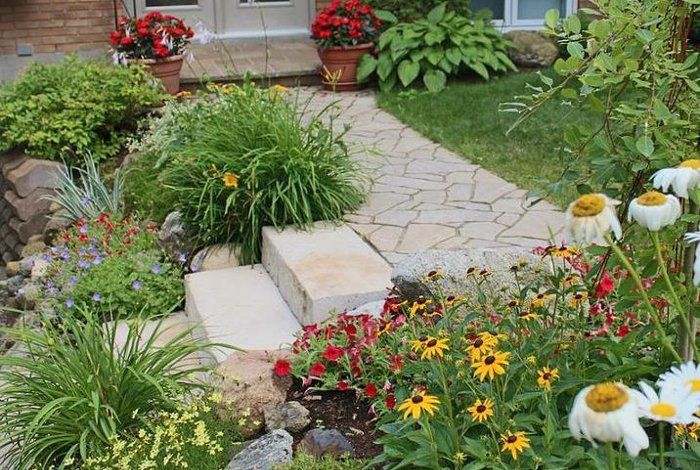 Allée de jardin en pierre entourée de fleurs colorées et d'une végétation luxuriante menant à l'entrée de la maison