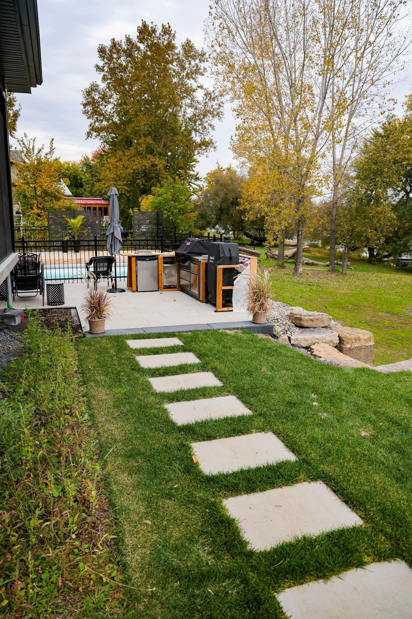 Terrasse arrière avec allée de pierres, pelouse verte et arbres d'automne entourant un coin salon extérieur