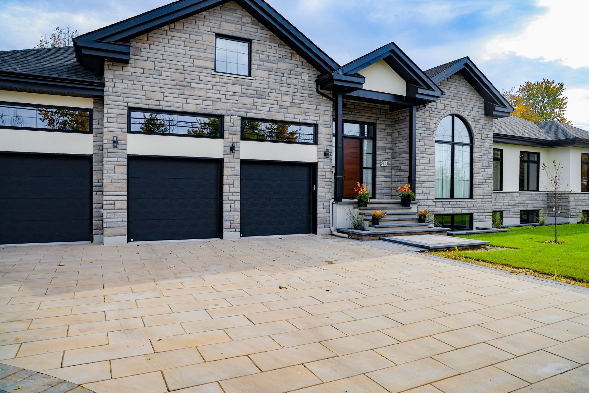 Maison moderne en pierre avec portes de garage noires et grande allée pavée