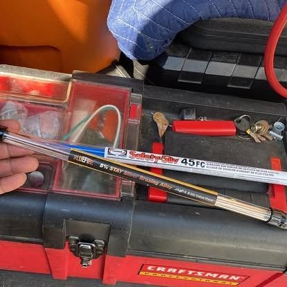 A hand holds two tubes of industrial brazing and soldering alloys over a red Craftsman toolbox.