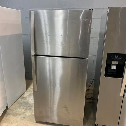 A stainless steel top-freezer refrigerator stands next to a stainless steel appliance with a water and ice dispenser.