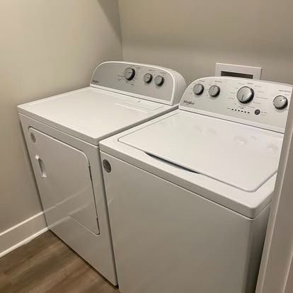 A white Whirlpool dryer and washing machine set in a corner with light gray walls and wood-look flooring.