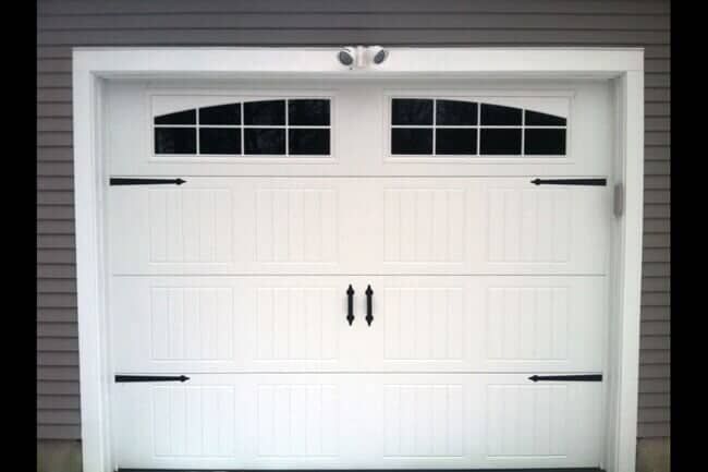 A white garage door with decorative black hinges and handles, and two rows of arched windows at the top.