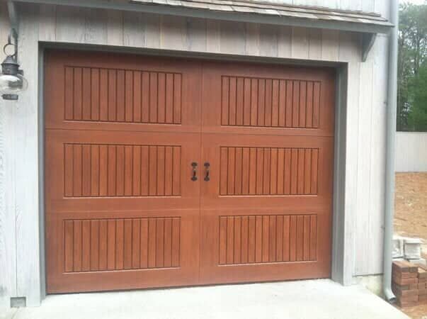 A brown, wooden sectional garage door with vertical slat panels and decorative black handles, set in a light frame.