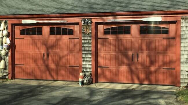 Two wooden garage doors with windows, each decorated with a horizontal white oar above the top panel.
