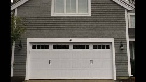 A two-story gray shingled house exterior featuring a white two-car garage door with window panels and the number 40 above.