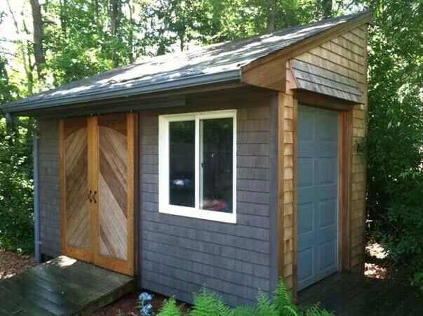 A wooden shed with dark shingles, a white-framed window, a double-door entrance, and a single blue door on the right.