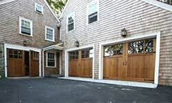 A tan shingled house with three wooden carriage-style garage doors on an asphalt driveway.