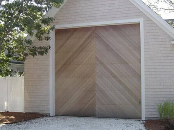 A large, single garage door with a chevron-patterned wood grain design set in a white-shingled building.