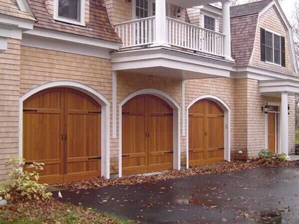 A large house exterior featuring three arched, natural wood garage doors and shingles on the siding.
