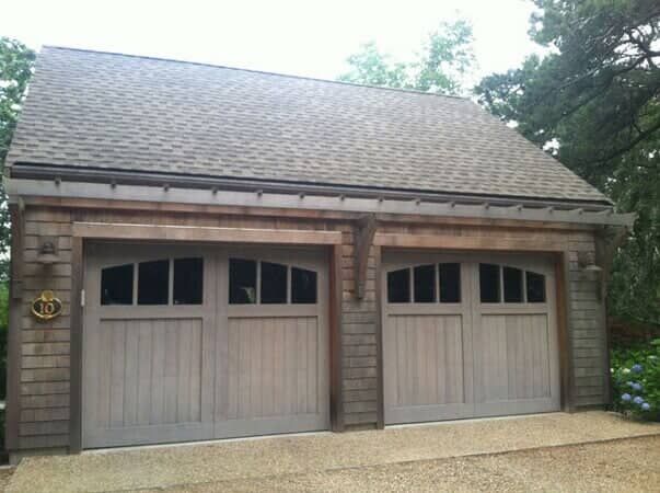 A detached two-car garage with shingled walls, a gabled roof, and two wooden garage doors with glass-pane windows.