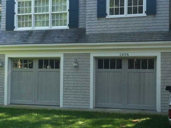A gray two-car garage with shingles and windows above each door on a residential house exterior.