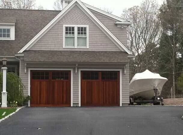 A gray-sided house with two brown carriage-style garage doors, with a boat on a trailer parked to the side.