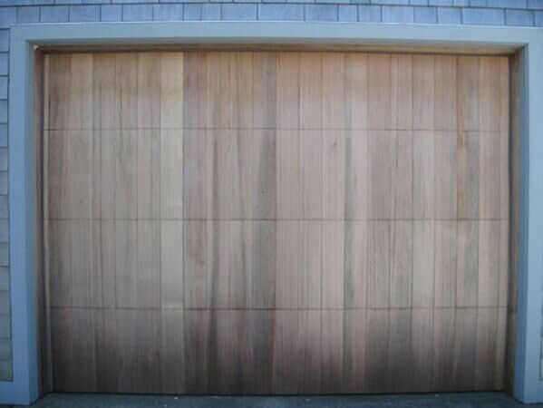 A wooden, horizontal panel garage door featuring vertical wood grain planks set within a gray frame.