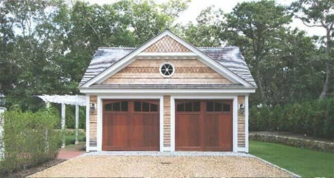 A detached two-car garage with natural cedar shingles, wood doors, a gabled roof, and a small round window.