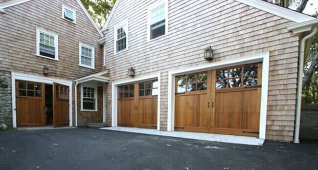 Shingle-sided home with a garage featuring three wood-paneled carriage-style doors and an open side entryway.