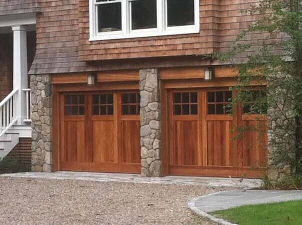 Two wooden carriage-style garage doors with windows set into a rustic stone and wood home exterior.