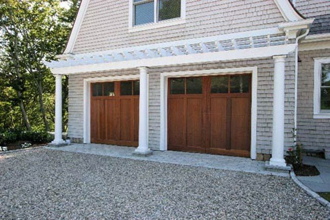 A two-car garage with wooden carriage-style doors, white columns, and a pergola under a shingled exterior.
