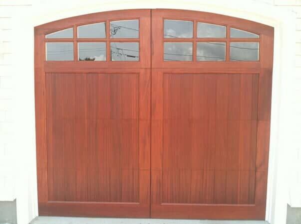 A wood garage door with an arched top and glass window panes arranged in two sections.