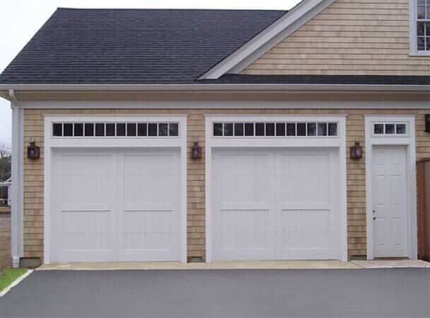 A two-car garage with shingled siding, white carriage-style doors with top windows, and a separate side entry door.
