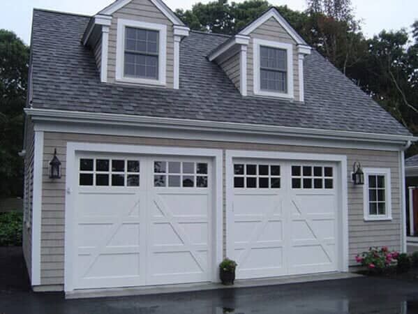Two-car garage with light gray shingle siding, white trim, carriage-style doors, and two dormer windows on the roof.