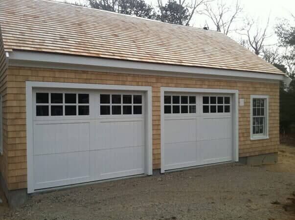 A two-car garage with shingled siding, white carriage-style doors, and a single window on a gravel driveway.