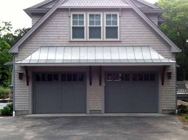A two-car garage with grey shingle siding, a metal shed roof, and three windows centered on the upper level.