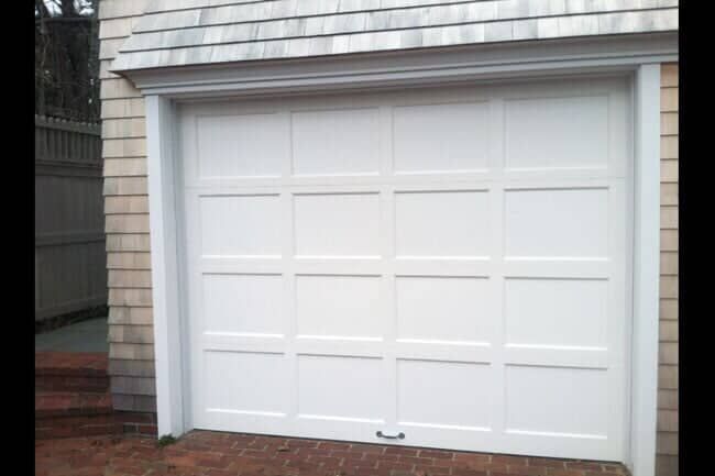 A white, four-panel residential garage door on a house with shingled siding.