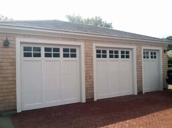 A detached garage with cedar shake siding and three white carriage-style doors with glass window panes at the top.