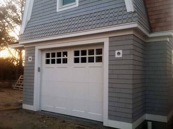 White garage door with windows on a gray, shingled building exterior at sunset.