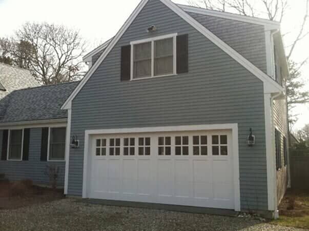 A light gray two-story garage with white trim and a white overhead garage door featuring rectangular window panels.