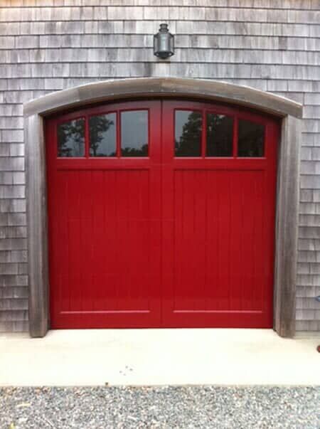 Bright red double garage doors with top windows set in a weathered wood-shingled building wall.